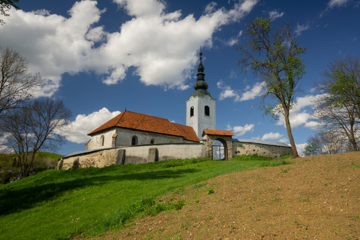 View of the historic Lutheran church with its white walls and tall black spire standing on a grassy hill under a blue sky in Rimavska Bana Banska Bystrica Regio Slovakia. View of the historic Lutheran church with its white walls and tall black spire standing on a grassy hill under a blue sky in Rimavska Bana Banska Bystrica Regio Slovakia.