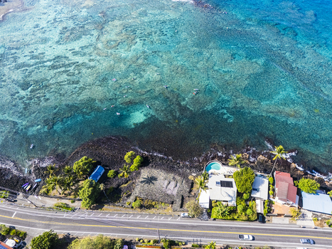 Aerial view of Kahalu u Beach Park featuring the turquoise coral reef volcanic rock coastline and coastal houses along the road in Kailua Kona Hawaii United States. Aerial view of Kahalu u Beach Park featuring the turquoise coral reef volcanic rock coastline and coastal houses along the road in Kailua Kona Hawaii United States.