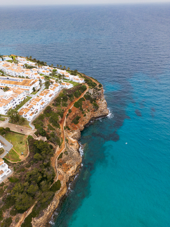 Aerial view of Cala Mendia featuring white resort buildings and rocky cliffs along the turquoise Mediterranean Sea in Cala Mendia Illes Balears Spain. Aerial view of Cala Mendia featuring white resort buildings and rocky cliffs along the turquoise Mediterranean Sea in Cala Mendia Illes Balears Spain.