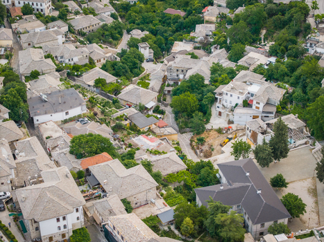 Aerial view of the historic stone roofed houses and narrow streets of the Gjirokaster old town surrounded by lush greenery in Gjirokaster Gjirokaster County Albania. Aerial view of the historic stone roofed houses and narrow streets of the Gjirokaster old town surrounded by lush greenery in Gjirokaster Gjirokaster County Albania.