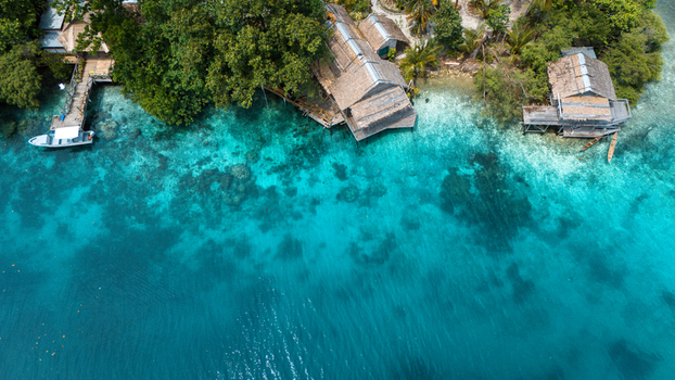 Aerial view of vibrant turquoise waters meet the lush green shoreline dotted with rustic huts and a wooden pier Solomon Islands Solomon Islands. Aerial view of vibrant turquoise waters meet the lush green shoreline dotted with rustic huts and a wooden pier Solomon Islands Solomon Islands.