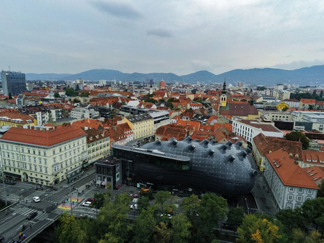 Aerial view of Kunsthaus Graz a contemporary art museum with a unique biomorphic architecture surrounded by historic red tiled rooftops and urban streets in Graz Styria Austria.