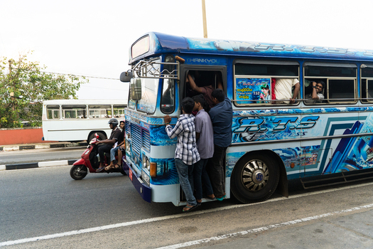 Sri Lanka 15 January 2026 View of a blue public transport bus with passengers hanging from the open door on a busy road.