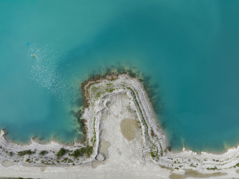 Aerial view of the turquoise waters of Aschheimer See with a sandy shoreline and sparse vegetation in Aschheim Bavaria Germany.