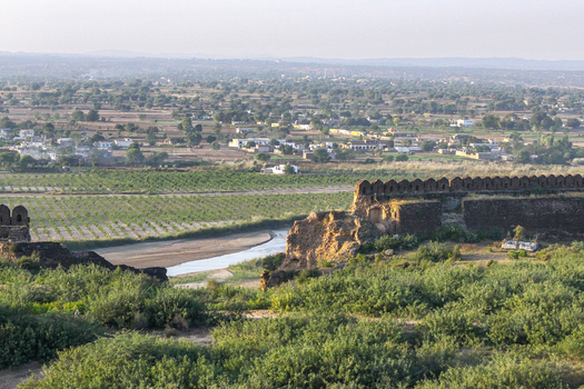 View of the historic stone walls of Rohtas Fort overlooking a winding stream agricultural fields and a distant town in Dina Punjab Pakistan. View of the historic stone walls of Rohtas Fort overlooking a winding stream agricultural fields and a distant town in Dina Punjab Pakistan.
