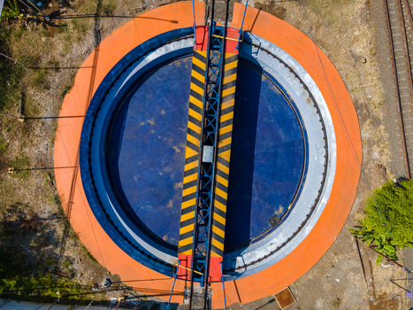 Aerial view of a railway turntable with a blue circular base an orange outer ring and a yellow and black striped bridge in Cilacap Central Java Indonesia. Aerial view of a railway turntable with a blue circular base an orange outer ring and a yellow and black striped bridge in Cilacap Central Java Indonesia.