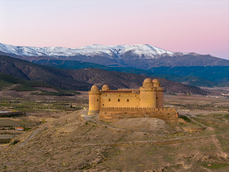 Aerial view of Castillo de La Calahorra standing on a hill with snow capped Sierra Nevada mountains in the background at sunset in La Calahorra Andalucia Spain. Aerial view of Castillo de La Calahorra standing on a hill with snow capped Sierra Nevada mountains in the background at sunset in La Calahorra Andalucia Spain.