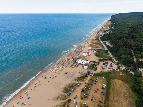 Aerial view of the sandy beach with rows of umbrellas a parking area and lush green forest bordering the Black Sea coastline in Shkorpilovtsi Varna Bulgaria. Aerial view of the sandy beach with rows of umbrellas a parking area and lush green forest bordering the Black Sea coastline in Shkorpilovtsi Varna Bulgaria.