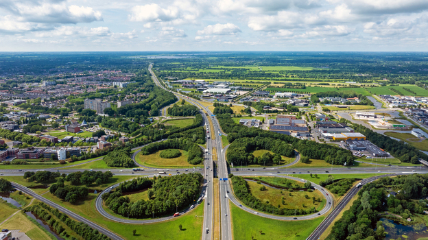 Aerial view of a highway interchange surrounded by lush green fields industrial buildings and residential areas in Drachten Friesland Netherlands.