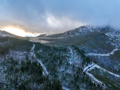 Aerial view of the snow dusted Serra da Estrela mountain range with winding roads and dense pine forests under a misty sky in Unhais da Serra Castelo Branco District Portugal. Aerial view of the snow dusted Serra da Estrela mountain range with winding roads and dense pine forests under a misty sky in Unhais da Serra Castelo Branco District Portugal.