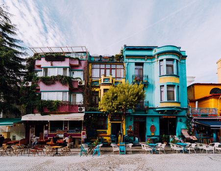 Istanbul Turkiye 07 October 2019 View of vibrant buildings with colorful facades create a lively street scene where tables and chairs sit on cobblestones under a bright sky.
