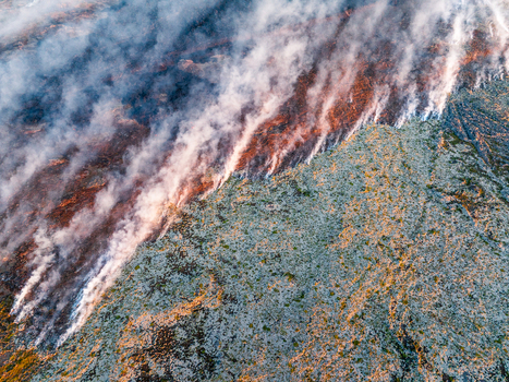 Aerial view of a volcanic eruption with molten lava flowing across a mossy landscape accompanied by thick plumes of smoke rising into the air in Iceland. Aerial view of a volcanic eruption with molten lava flowing across a mossy landscape accompanied by thick plumes of smoke rising into the air in Iceland.