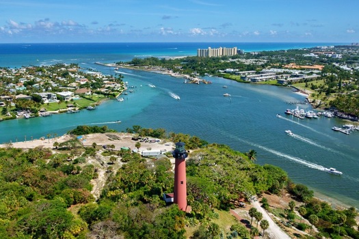 Aerial view of the Jupiter Inlet Lighthouse overlooking the turquoise waters of the inlet with boats cruising past lush coastal greenery in Jupiter Florida United States. Aerial view of the Jupiter Inlet Lighthouse overlooking the turquoise waters of the inlet with boats cruising past lush coastal greenery in Jupiter Florida United States.