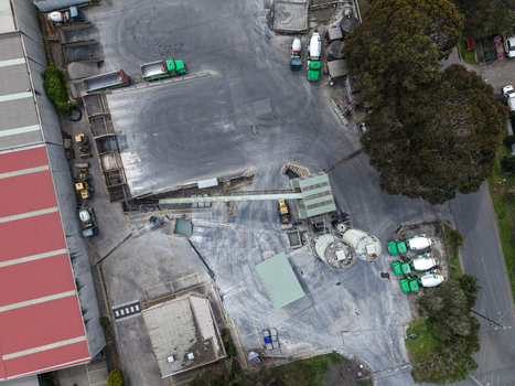 Melbourne VIC Australia 25 September 2026 Aerial view of an industrial facility featuring concrete silos heavy machinery and parked trucks on a paved yard.