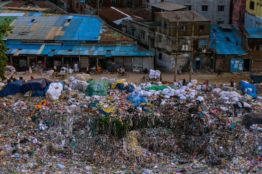 Aerial view of a massive garbage dump with piles of plastic waste and sacks near residential buildings with blue roofs in Keraniganj Dhaka Division Bangladesh. Aerial view of a massive garbage dump with piles of plastic waste and sacks near residential buildings with blue roofs in Keraniganj Dhaka Division Bangladesh.