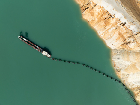 Aerial view of a dredging vessel operating in a turquoise quarry lake with a floating pipeline extending towards the sandy banks in Coimbra Coimbra District Portugal. Aerial view of a dredging vessel operating in a turquoise quarry lake with a floating pipeline extending towards the sandy banks in Coimbra Coimbra District Portugal.