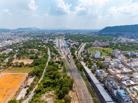 Aerial view of Udaipur Railway Station with multiple tracks surrounding urban buildings lush green trees and distant hills under a bright blue sky in Udaipur Rajasthan India. Aerial view of Udaipur Railway Station with multiple tracks surrounding urban buildings lush green trees and distant hills under a bright blue sky in Udaipur Rajasthan India.