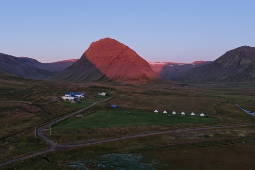 Aerial view of the dramatic mountain landscape near Flateyri at sunset featuring a small cluster of buildings and white tents in Flateyri Isafjardarbaer Iceland. Aerial view of the dramatic mountain landscape near Flateyri at sunset featuring a small cluster of buildings and white tents in Flateyri Isafjardarbaer Iceland.