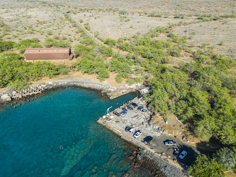 Aerial view of Mahukona Beach Park with its rocky coastline turquoise waters and a small pier with parked vehicles in Waimea Hawaii United States.
