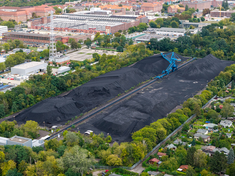 Aerial view of a large coal storage area with a mechanical stacker surrounded by industrial buildings and residential greenery in Berlin Berlin Germany.