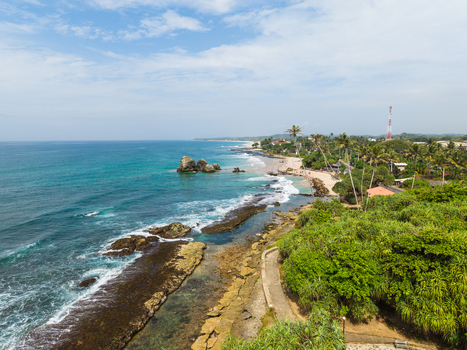 Aerial view of the tropical coastline with turquoise waves crashing against rocky shores and lush palm trees Koggala Southern Province Sri Lanka. Aerial view of the tropical coastline with turquoise waves crashing against rocky shores and lush palm trees Koggala Southern Province Sri Lanka.