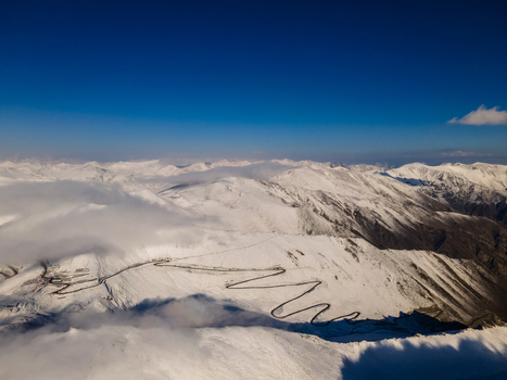 Aerial view of the winding road of Babusar Pass through snow covered mountain peaks under a clear blue sky in Babusar KPK Pakistan.