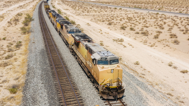 Aerial view of a freight train moving along tracks through a vast arid desert landscape in the United States.