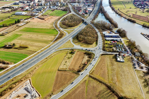 Aerial view of a highway interchange with cars driving through green fields and industrial areas next to a river in Forchheim Bavaria Germany. Aerial view of a highway interchange with cars driving through green fields and industrial areas next to a river in Forchheim Bavaria Germany.