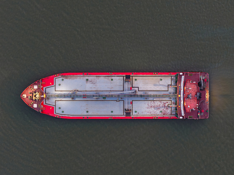 Aerial view of a cargo ship navigating the Mahakam River with a red hull and metallic deck in the calm water of Samarinda East Kalimantan Indonesia. Aerial view of a cargo ship navigating the Mahakam River with a red hull and metallic deck in the calm water of Samarinda East Kalimantan Indonesia.