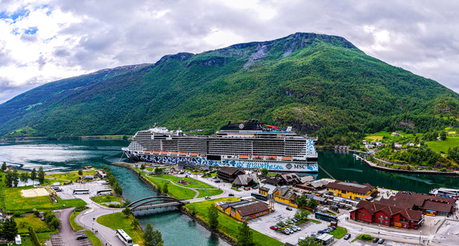 Flam Norway 18 June 2026 Aerial view of a large cruise ship docked in the fjord at Flam surrounded by lush green mountains a river and small buildings. Flam Norway 18 June 2026 Aerial view of a large cruise ship docked in the fjord at Flam surrounded by lush green mountains a river and small buildings.