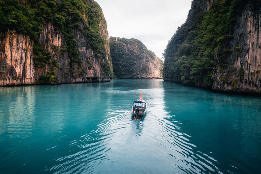 Aerial view of Pi Leh Bay featuring a traditional long tail boat navigating through turquoise waters surrounded by towering limestone cliffs in Tambon Ao Nang Chang Wat Krabi Thailand. Aerial view of Pi Leh Bay featuring a traditional long tail boat navigating through turquoise waters surrounded by towering limestone cliffs in Tambon Ao Nang Chang Wat Krabi Thailand.