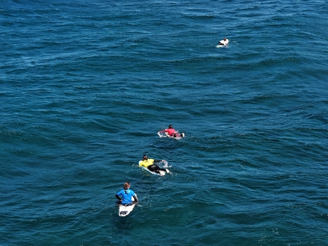 Aerial view of surfers paddling on their boards in the deep blue ocean water at Praia do Areal de Santa Barbara Ribeira Grande Acores Portugal. Aerial view of surfers paddling on their boards in the deep blue ocean water at Praia do Areal de Santa Barbara Ribeira Grande Acores Portugal.