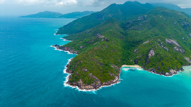 Aerial view of lush green coastal headland of Cap Ternay with rocky cliffs turquoise water and a secluded sandy beach in Cap Ternay Port Glaud Seychelles. Aerial view of lush green coastal headland of Cap Ternay with rocky cliffs turquoise water and a secluded sandy beach in Cap Ternay Port Glaud Seychelles.