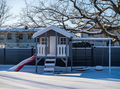 View of a wooden playhouse with a slide and swings covered in fresh snow in a backyard in Vilnius Vilnius County Lithuania. View of a wooden playhouse with a slide and swings covered in fresh snow in a backyard in Vilnius Vilnius County Lithuania.