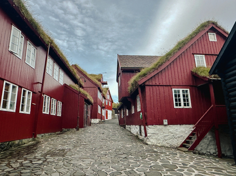 View of traditional red wooden houses with grass roofs lining a narrow cobblestone street in the Faroe Islands. View of traditional red wooden houses with grass roofs lining a narrow cobblestone street in the Faroe Islands.