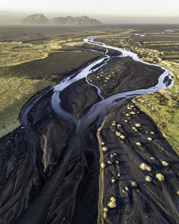 Aerial view of a braided glacial river winding through black volcanic sand plains and mossy fields under a soft morning light in Myrdalshreppur Myrdalshreppur Iceland.