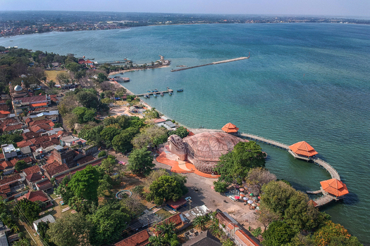 Aerial view of the giant turtle shaped building of Kura Kura Ocean Park on the coastline with blue sea and urban rooftops in Jepara Central Java Indonesia. Aerial view of the giant turtle shaped building of Kura Kura Ocean Park on the coastline with blue sea and urban rooftops in Jepara Central Java Indonesia.