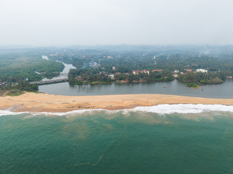Aerial view of a coastal landscape featuring a sandy beach a river estuary and dense tropical greenery under a misty sky in Galle Southern Province Sri Lanka.