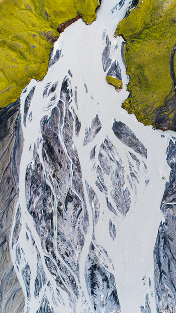 Aerial view of the braided glacial river at Thakgil with sediment rich water flowing through vibrant green mossy terrain in Vik Myrdalshreppur Iceland.