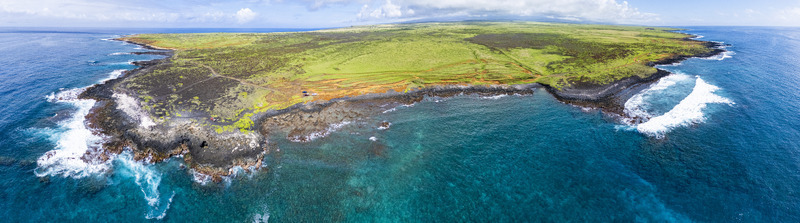 Aerial view of Kalae coastline featuring volcanic rock formations turquoise ocean waters and lush green fields under a bright sky Hawaii County Hawaii United States. Aerial view of Kalae coastline featuring volcanic rock formations turquoise ocean waters and lush green fields under a bright sky Hawaii County Hawaii United States.