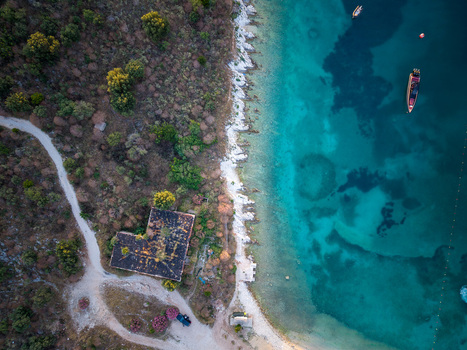 Aerial view of the rocky coastline with turquoise water a dirt road and small boats near the shore in Porto Palermo Qarku i Vlores Albania. Aerial view of the rocky coastline with turquoise water a dirt road and small boats near the shore in Porto Palermo Qarku i Vlores Albania.