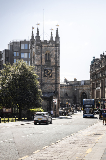 Newcastle upon Tyne United Kingdom 13 July 2026 View of St Nicholas Cathedral with a clock tower historic stone architecture a passing bus and a car on a city street. Newcastle upon Tyne United Kingdom 13 July 2026 View of St Nicholas Cathedral with a clock tower historic stone architecture a passing bus and a car on a city street.