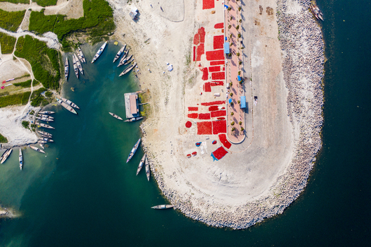 Bogura Bangladesh 06 March 2022 Aerial view of wooden boats docked along the riverbank with vibrant red chilies spread out to dry on the concrete embankment.