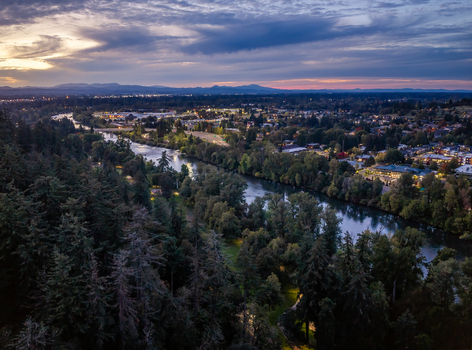 Aerial view of the Willamette River winding through Eugene at twilight with city lights dense surrounding forests and a colorful sunset sky in Eugene Oregon United States. Aerial view of the Willamette River winding through Eugene at twilight with city lights dense surrounding forests and a colorful sunset sky in Eugene Oregon United States.