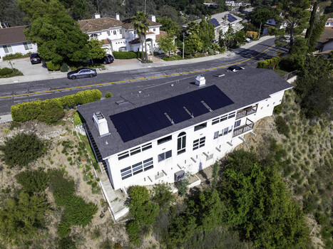 Aerial view of a modern white house on a hillside with a large solar panel array on the roof surrounded by lush greenery in Los Angeles California United States. Aerial view of a modern white house on a hillside with a large solar panel array on the roof surrounded by lush greenery in Los Angeles California United States.