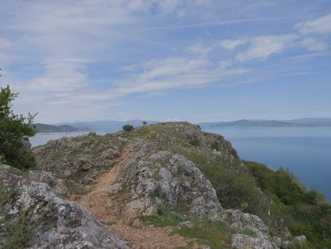 View of the rocky peninsula of Lin extending into Lake Ohrid with a dirt path sparse vegetation and distant mountains under a blue sky in Lin Korce County Albania.
