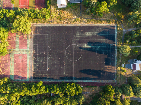 Aerial view of an old weathered soccer field with visible white markings surrounded by lush green trees and adjacent sports courts in Kiten Burgas Bulgaria. Aerial view of an old weathered soccer field with visible white markings surrounded by lush green trees and adjacent sports courts in Kiten Burgas Bulgaria.