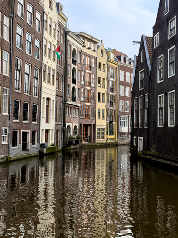 View of traditional narrow canal houses with colorful facades reflecting in the calm water under a cloudy sky in Amsterdam North Holland Netherlands. View of traditional narrow canal houses with colorful facades reflecting in the calm water under a cloudy sky in Amsterdam North Holland Netherlands.