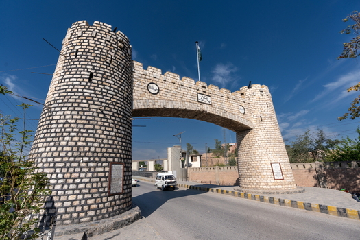 View of the historic Khyber Pass stone archway and towers with a vehicle passing through under a clear blue sky in Khyber District Khyber Pakhtunkhwa Pakistan.