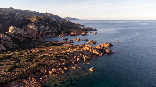 Aerial view of Cala Sarraina featuring rugged rocky cliffs turquoise waters and Mediterranean scrub along the coastline at golden hour in Trinita d Agultu e Vignola Sardinia Italy. Aerial view of Cala Sarraina featuring rugged rocky cliffs turquoise waters and Mediterranean scrub along the coastline at golden hour in Trinita d Agultu e Vignola Sardinia Italy.